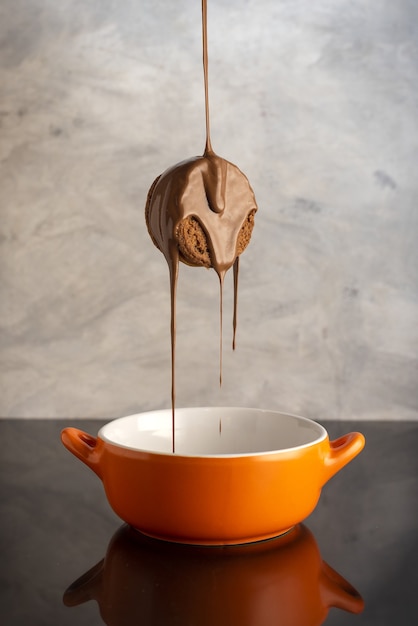 Vertical shot of a tasty biscuit being covered by chocolate over an orange bowl