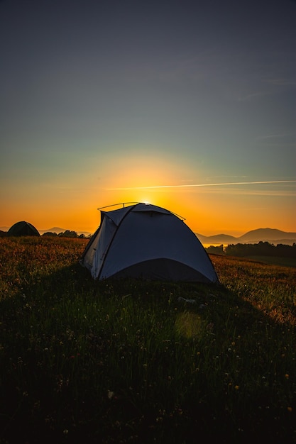 Vertical shot of a tent on a hill covered in greenery during a beautiful sunrise in the morning