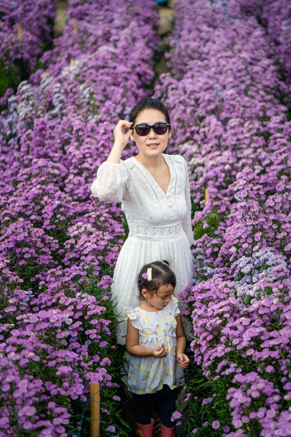 들판에서 보라색 제라툼 꽃을 즐기는 태국 엄마와 딸의 세로 샷
