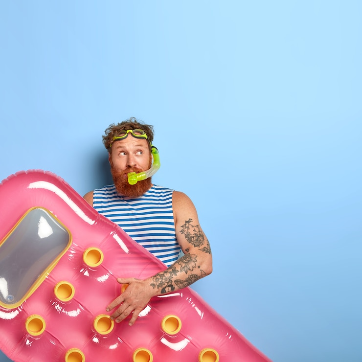 Free Photo vertical shot of thoughtful redhead guy wears snorkeling mask, enjoys swimming and resting, holds pink inflated mattress