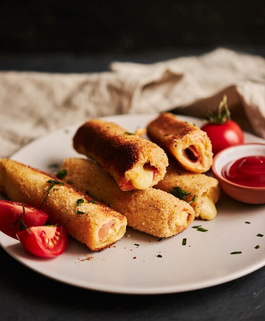 Vertical shot of toast rolls with ham and cheese and tomatoes and ketchup on a white plate