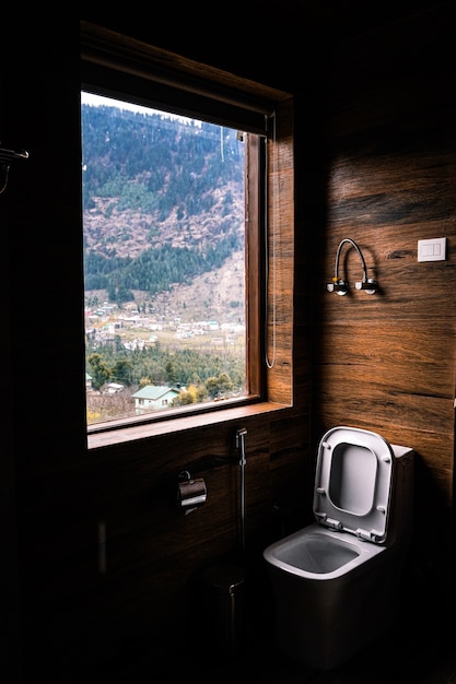 Vertical shot of a toilet seat by the window with the beautiful view of a landscape