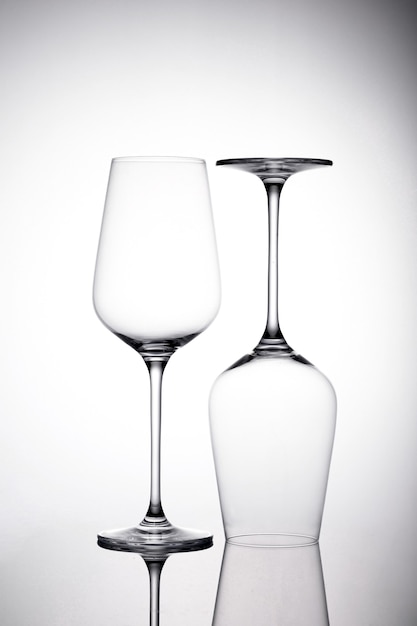 影のある白い表面に2つの空のワイングラスの垂直ショット、1つは逆さまです
