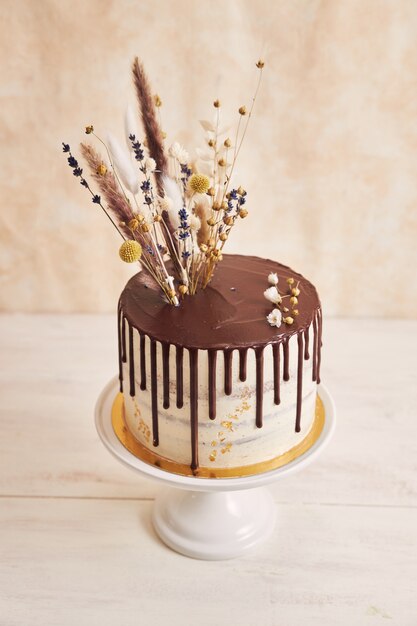 Vertical shot of a vanilla cake with chocolate drip and flowers on top