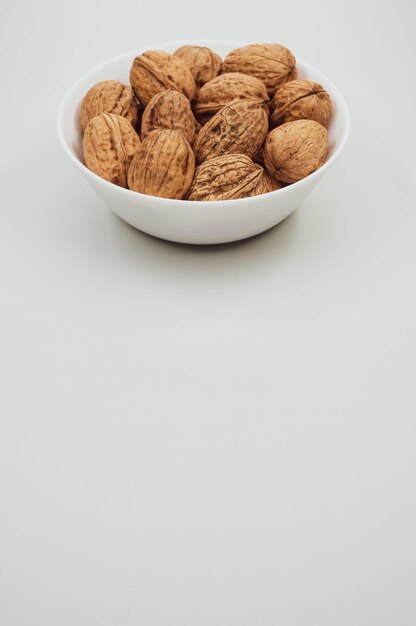 Вертикальный снимок грецких орехов на белой миске на белом фоне