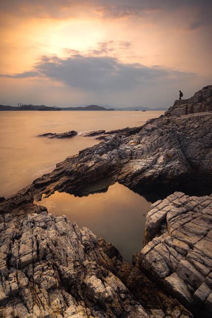 Vertical shot of the water and the cliffs during a sunset in a clouded sky