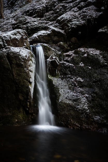 Ripresa verticale di una cascata che esce da un'enorme roccia coperta di neve nella stagione invernale winter