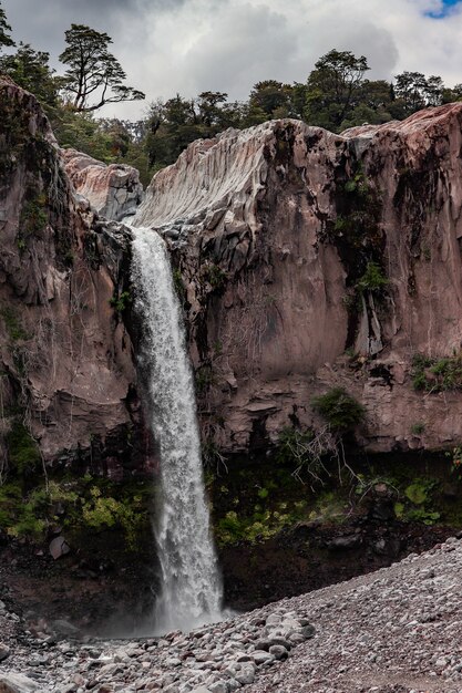 Vertical shot of a waterfall in the middle of cliffs under a cloudy sky