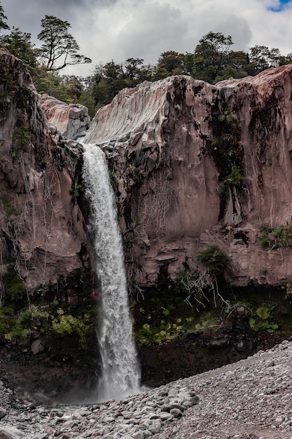 Vertical shot of a waterfall in the middle of cliffs under a cloudy sky