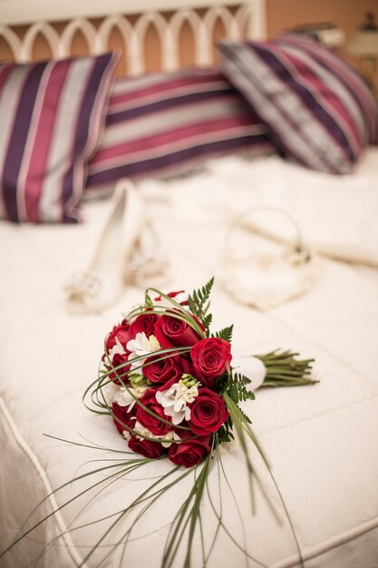 Вертикальный снимок свадебного букета с красными розами на кровати