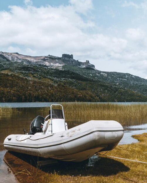Вертикальный снимок белой лодки, припаркованной в озере, на фоне горы