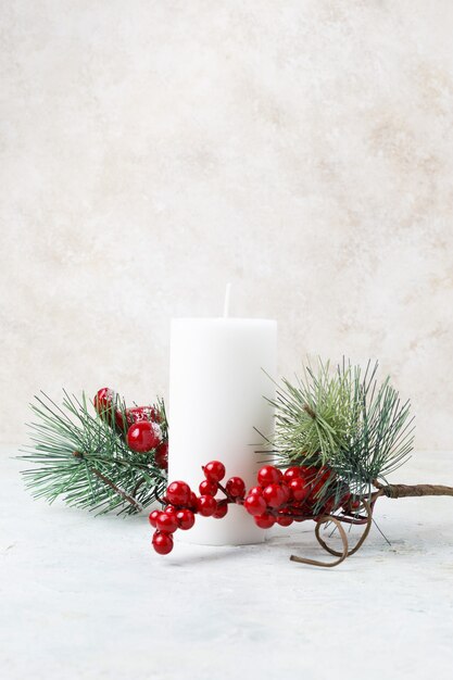 Vertical shot of a white candle surrounded by Christmas hollies and leaves on a white marble surface