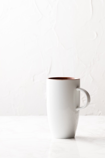 Vertical shot of a white ceramic cup on a white surface