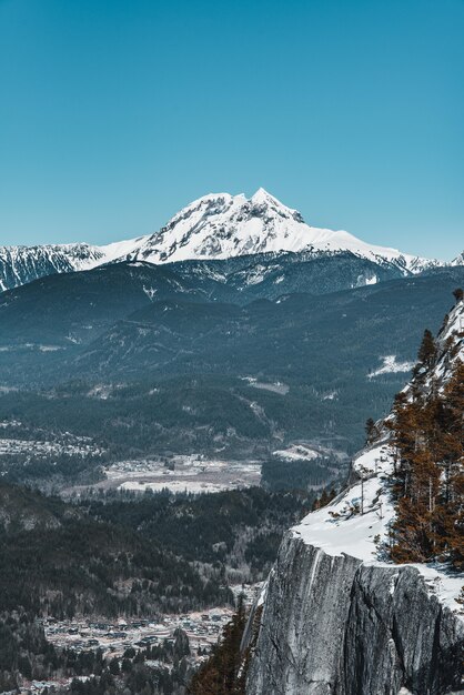 Vertical shot of a white mountain surrounded by trees and cliffs under a blue sky