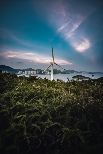 Vertical shot of a wind turbine in a field with the sea in the background