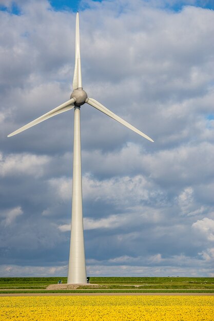 Vertical shot of a windmill on a grassy field with a cloudy sky in the background