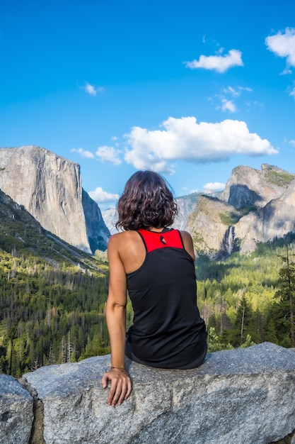 Вертикальный снимок женщины, сидящей на камне в национальном парке Йосемити в США