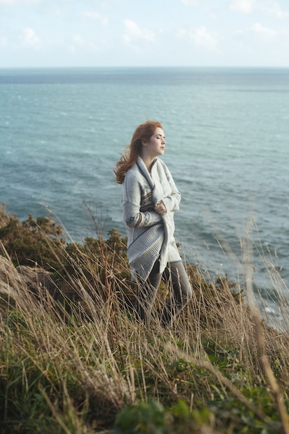 Free photo vertical shot of a woman standing on the shore with the sea on the background