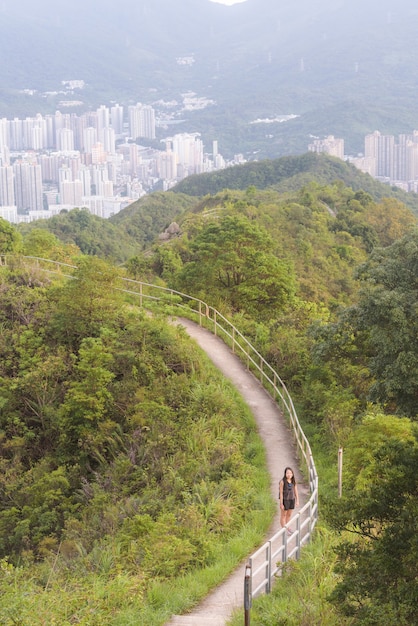 나무와 녹지로 둘러싸인 좁은 길을 걷는 여성의 세로 샷