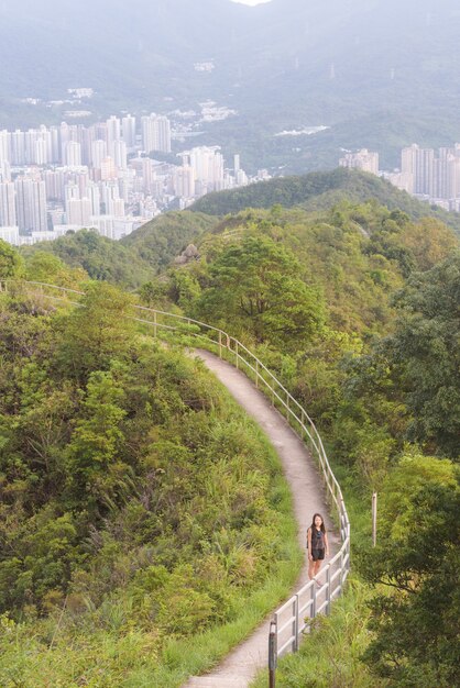 Vertical shot of a woman walking on a narrow path surrounded by trees and greenery