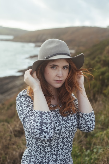 Vertical shot of a woman wearing a hat with the sea and trees