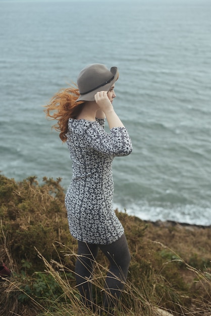 Vertical shot of a woman wearing a hat with the sea