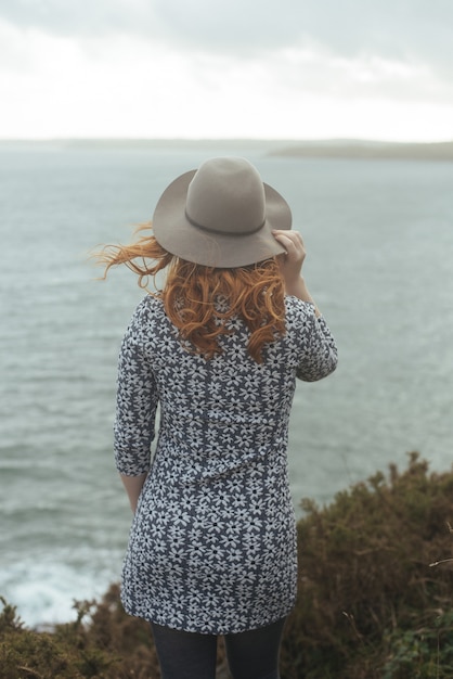 Vertical shot of a woman wearing a hat with the sea