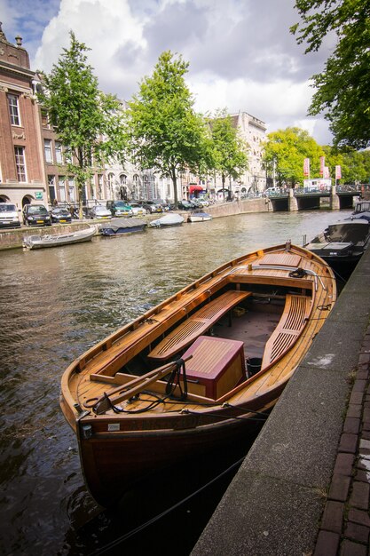 Vertical shot of wooden boats by the canal surrounded by houses captured in Amsterdam, Netherlands
