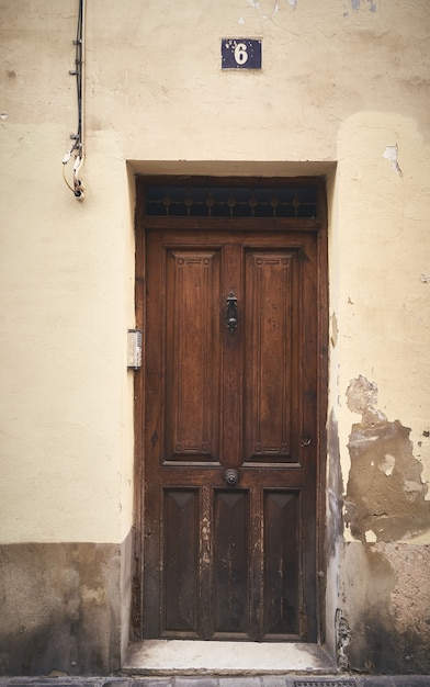 A vertical shot of a wooden door with the number 6 above it