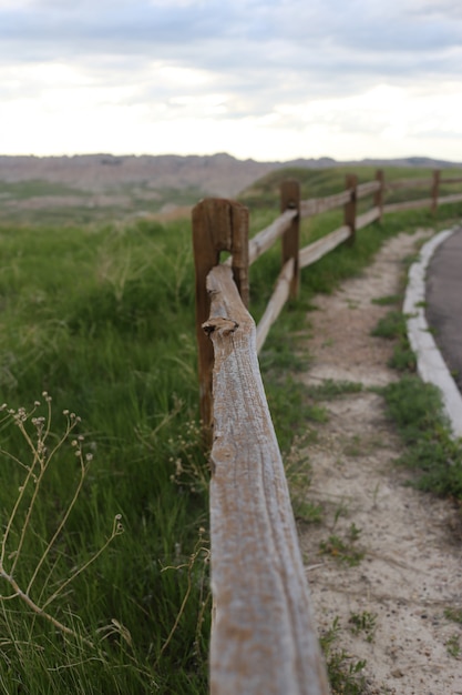 Vertical shot of a wooden fence in the middle of a road and a grass field