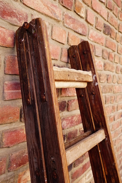 Vertical shot of a wooden foldable ladder leaned against a brick wall