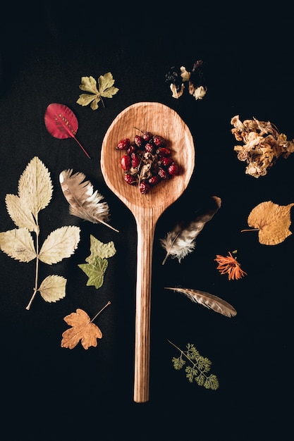 Free photo vertical shot of a wooden spoon surrounded with different plants leaves and feathers