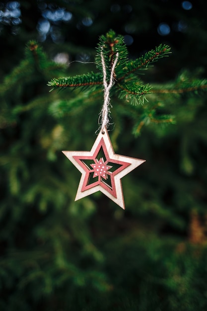 Vertical shot of a wooden star-shaped Christmas ornament hanging from a pine tree