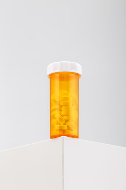 Vertical shot of a yellow container filled with pills on a white table