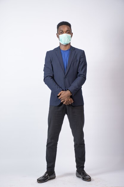 Vertical shot of a young black businessman wearing a suit and also a face mask, standing confidently