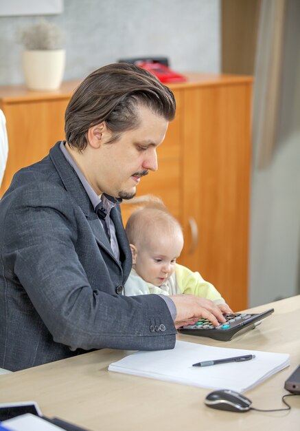 Vertical shot of a young businessman working from his office and holding a baby