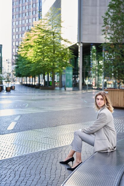 Foto gratuita il colpo verticale di una giovane donna d'affari in abito beige si gira in attesa di qualcuno fuori dall'ufficio bu