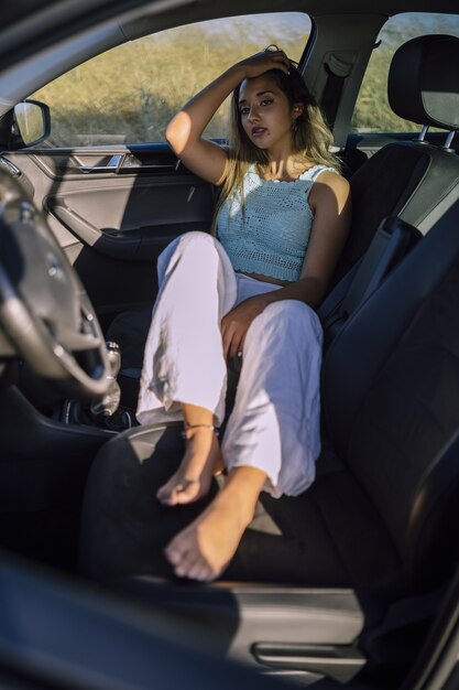 Vertical shot of a young caucasian female posing in the front seat of a car in a field