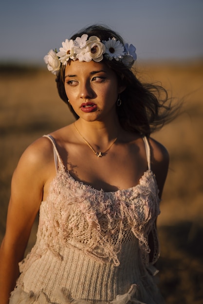 Vertical shot of a young caucasian female in white dress and white flower wreath posing in a field