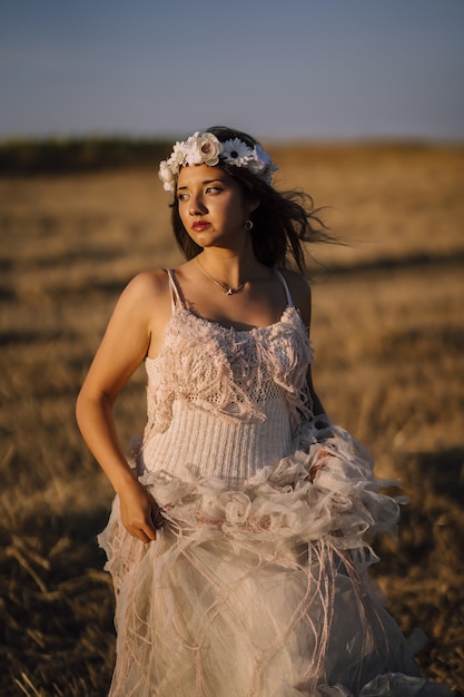 野原でポーズをとる白いドレスと白い花の花輪の若い白人女性の垂直ショット