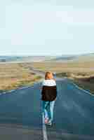 Free photo vertical shot of a young female in jeans walking in the highway