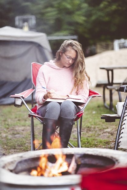Vertical shot of a young female studying outdoors in front of a fire