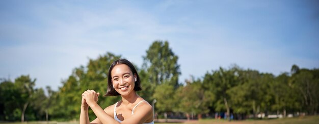 Free Photo vertical shot of young fit woman does squats in park using stretching band on legs smiling pleased