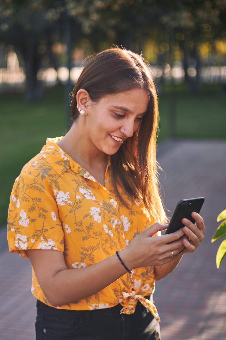 Free Photo vertical shot of a young girl in a yellow shirt looking at her phone and smiling