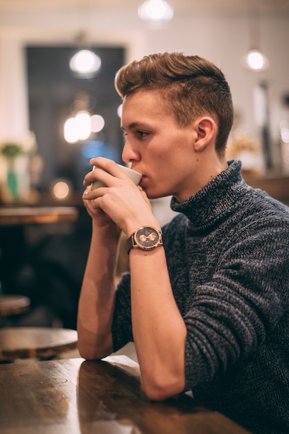 Вертикальный снимок молодого человека, пьющего кофе в кафе