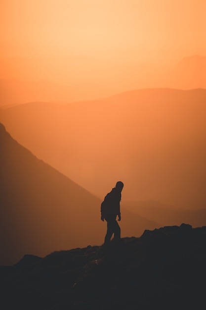 Vertical silhouette of a person climbing up the hill at sunset