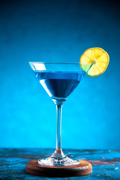 Vertical view of alchocol cocktail in a glass goblet served with lemon slice on blue background
