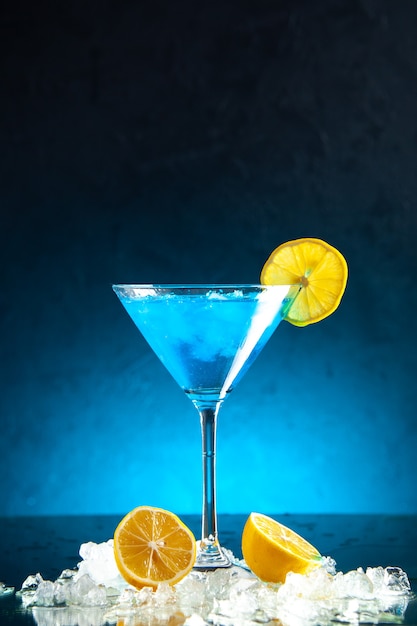 Вертикальный вид алкогольный коктейль в стеклянном кубке, подается со льдом из дольки лимона на синем фоне
