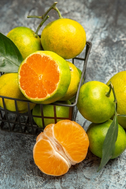 Free photo vertical view of a basket full of fresh green tangerines and cut in half tangerine on gray background