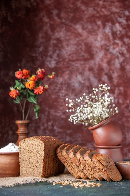 Вертикальный вид муки из ломтиков черного хлеба в миске и пшеницы на полотенце телесного цвета и цветочных горшках на фоне смешанных цветов
